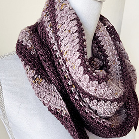 A close up show of a pink and purple crocheted shawl on a mannequin