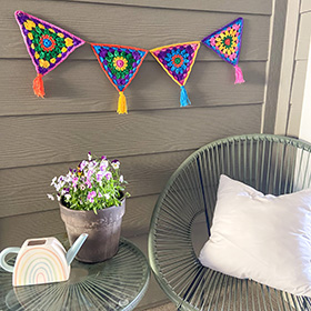 Hanging colorful crochet granny squares on a porch with chairs and a plant