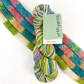 A blue and green colorful skein of yarn laying on a knit sample of the same yarn